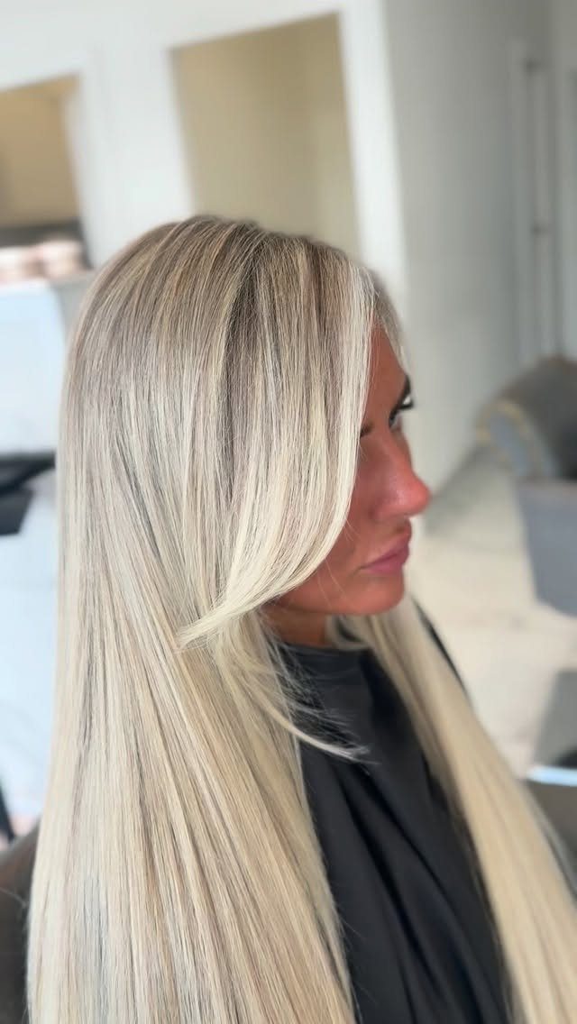 Long creamy platinum blonde hair with darker roots, worn straight in a salon