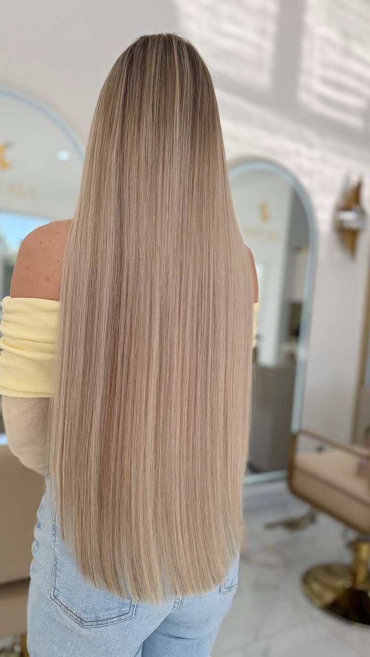Long straight natural blonde hair falls down the back in a salon.