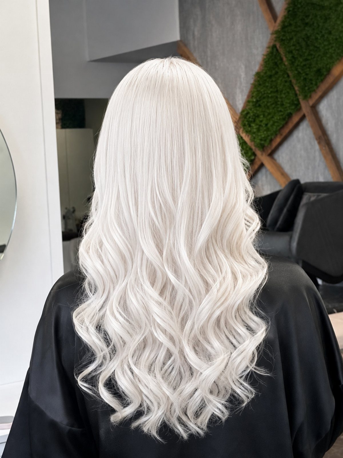 Long pale creamy blonde hair styled in loose waves over a black salon cape