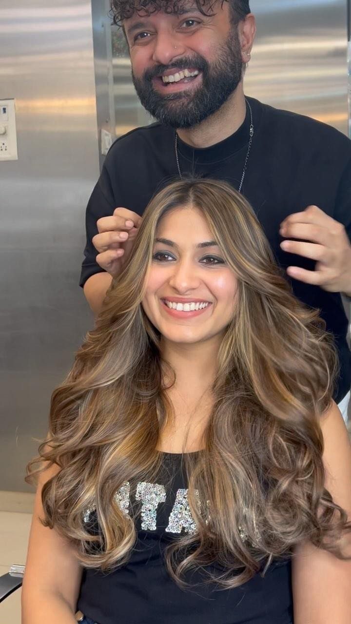 Woman with wavy brown balayage highlights sits smiling in a salon
