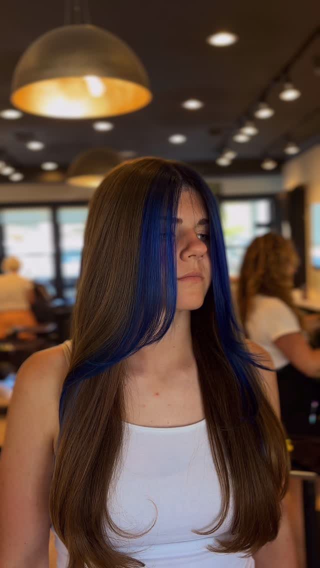 Long brown hair with vivid blue face-framing highlights in a salon