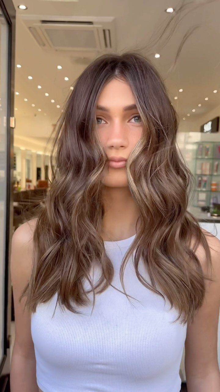 Woman with long wavy brown hair and lighter caramel-toned highlights in a salon