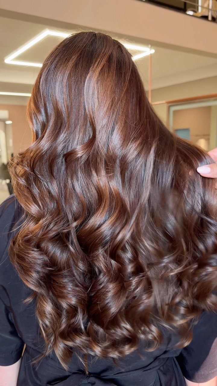 Long chocolate-brown highlighted hair styled in glossy, loose curls