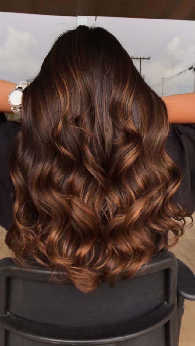 Long curled dark brown hair with warm copper highlights styled in a salon chair