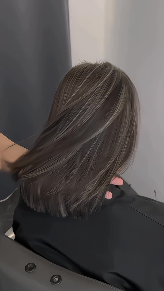 Dark brown hair with fine silver-gray highlights rests over a black salon cape
