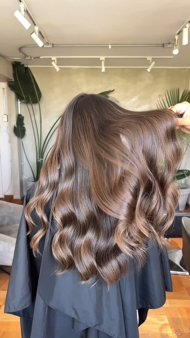 Wavy brown hair with subtle, natural-looking lighter highlights in a salon
