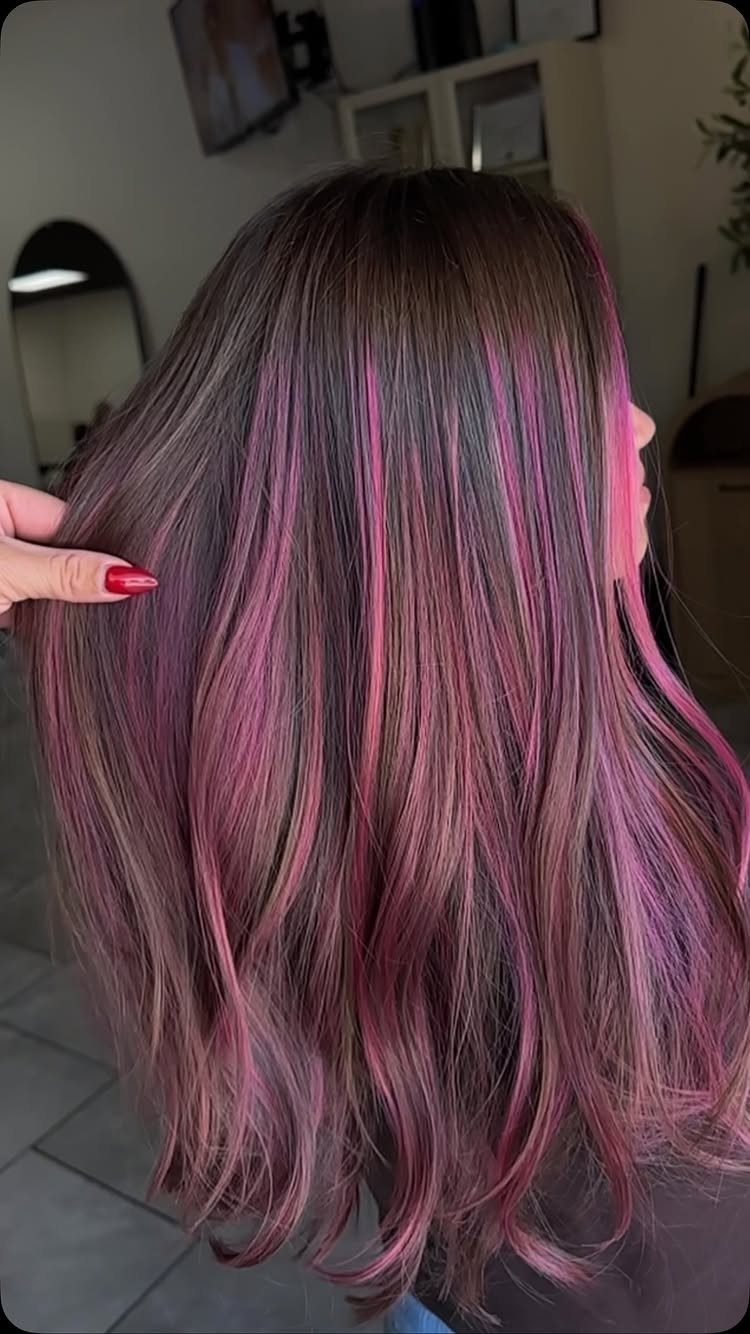 Dark brown wavy hair with pink highlights displayed in a salon