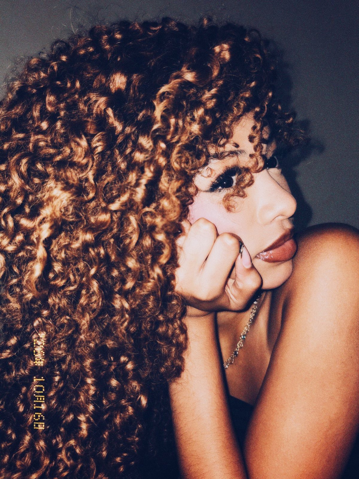 Woman posing with long dark brown curls and golden highlights