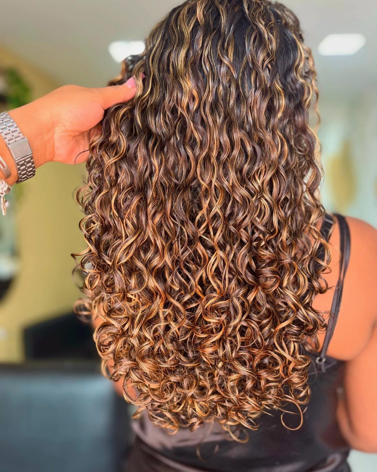 Brunette curls with golden highlights lifted by a hand in a salon