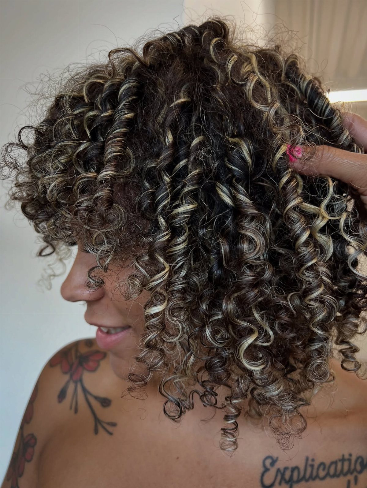 Highlighted tight curls with blonde and light brown strands, shown in profile