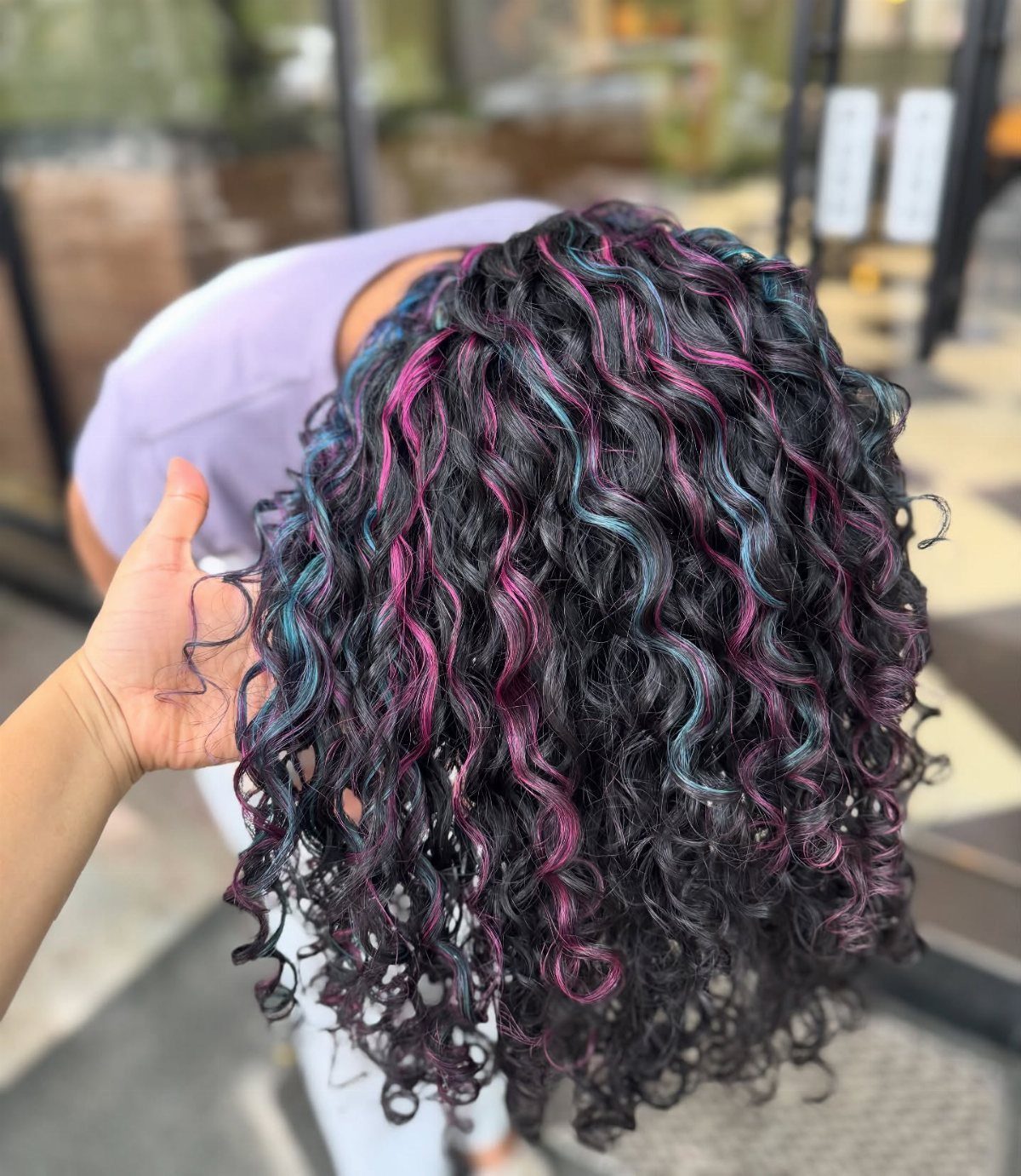 Dark curly hair with vivid pink and teal streaks in a salon