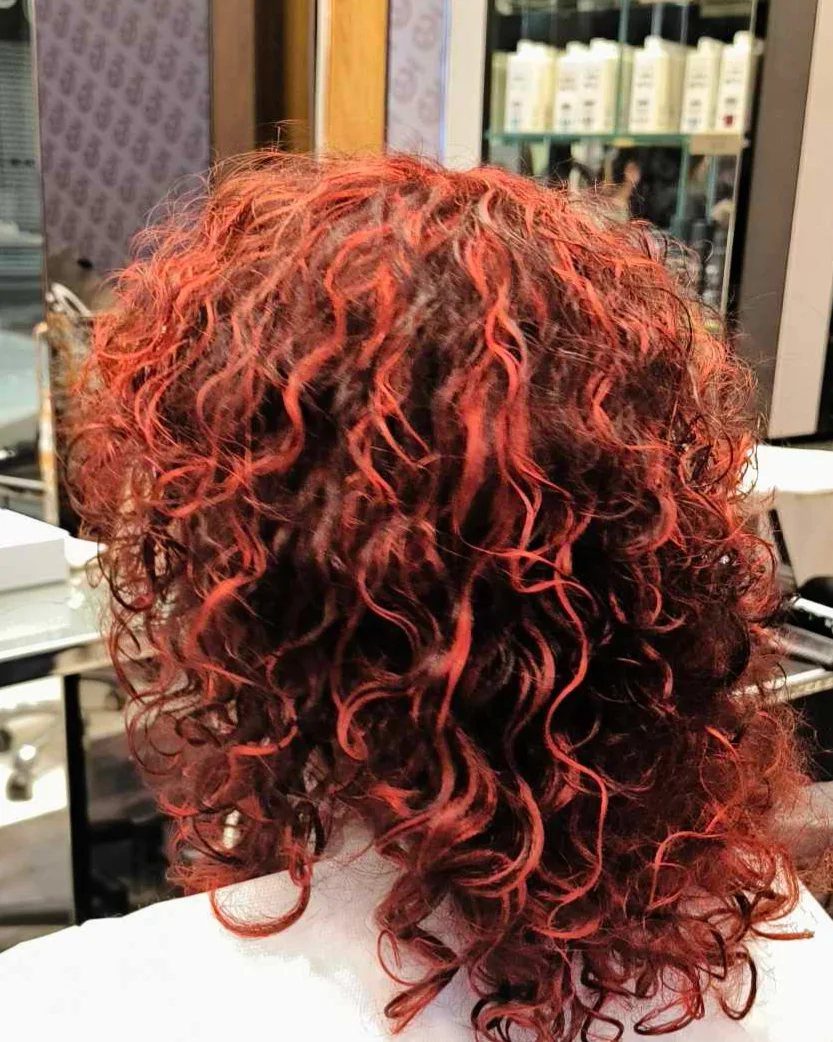 Black curls with vivid red highlights shown from behind in a salon