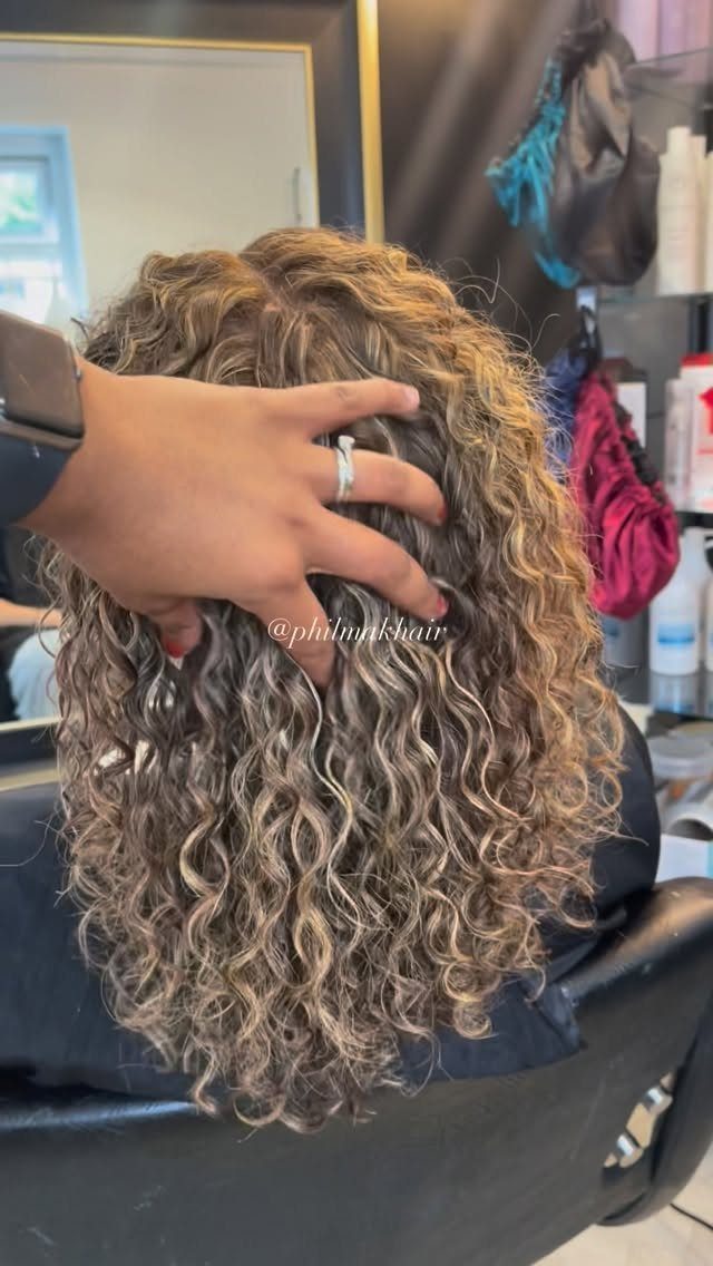 Long curly hair with lightened strands being parted by a stylist in a salon