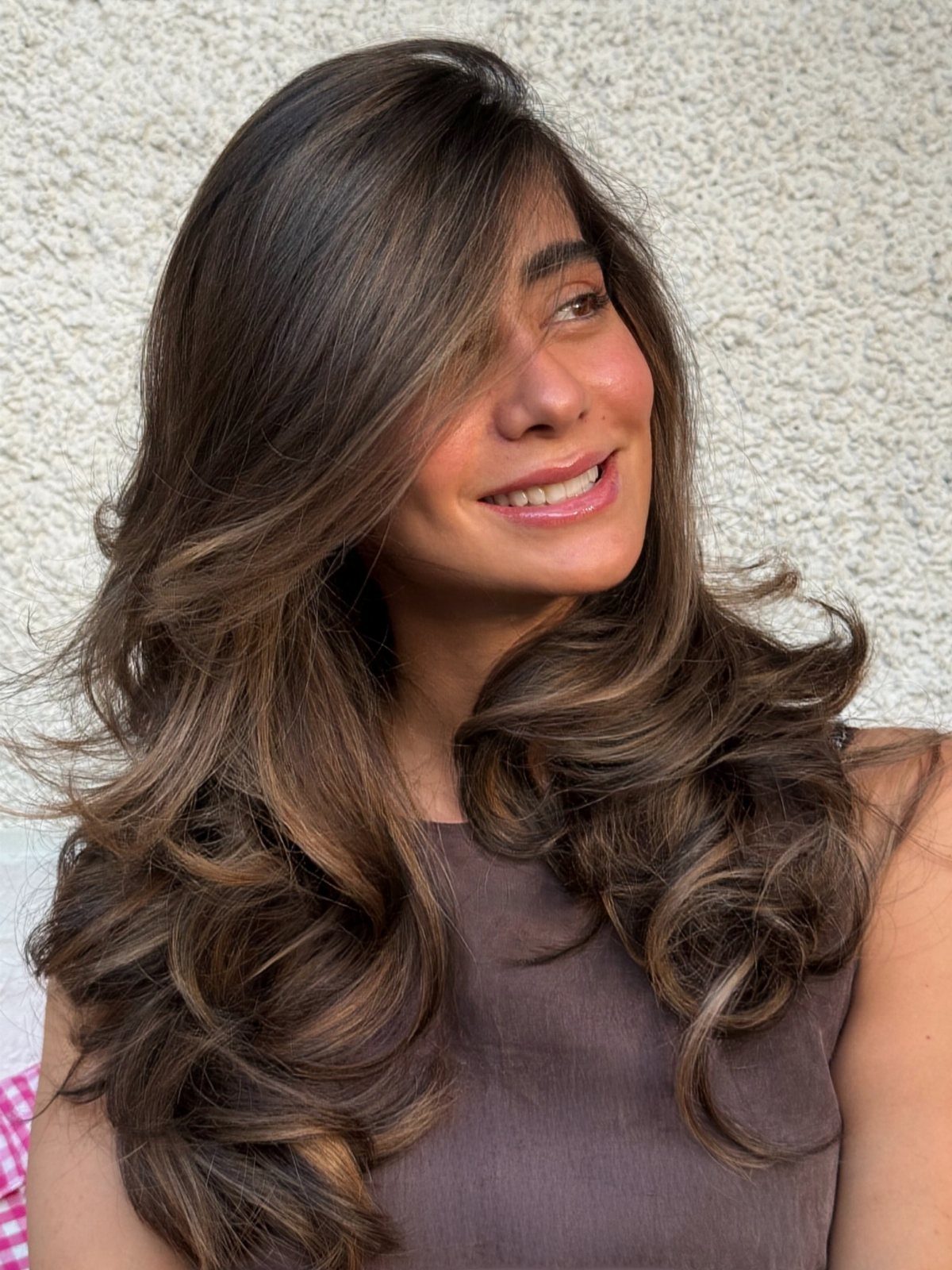 Woman with long wavy cool brunette hair and subtle lighter strands