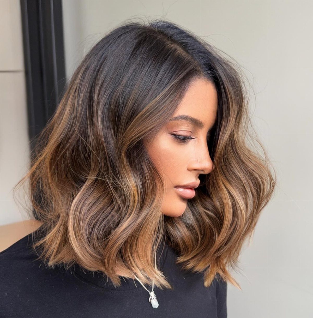 Wavy dark brown lob with amber highlights framing a woman's face