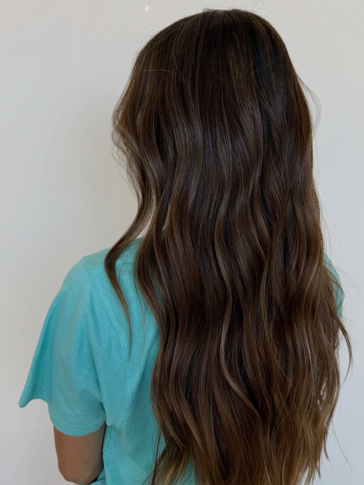 Long glossy chocolate brunette hair falls in soft waves over a turquoise top