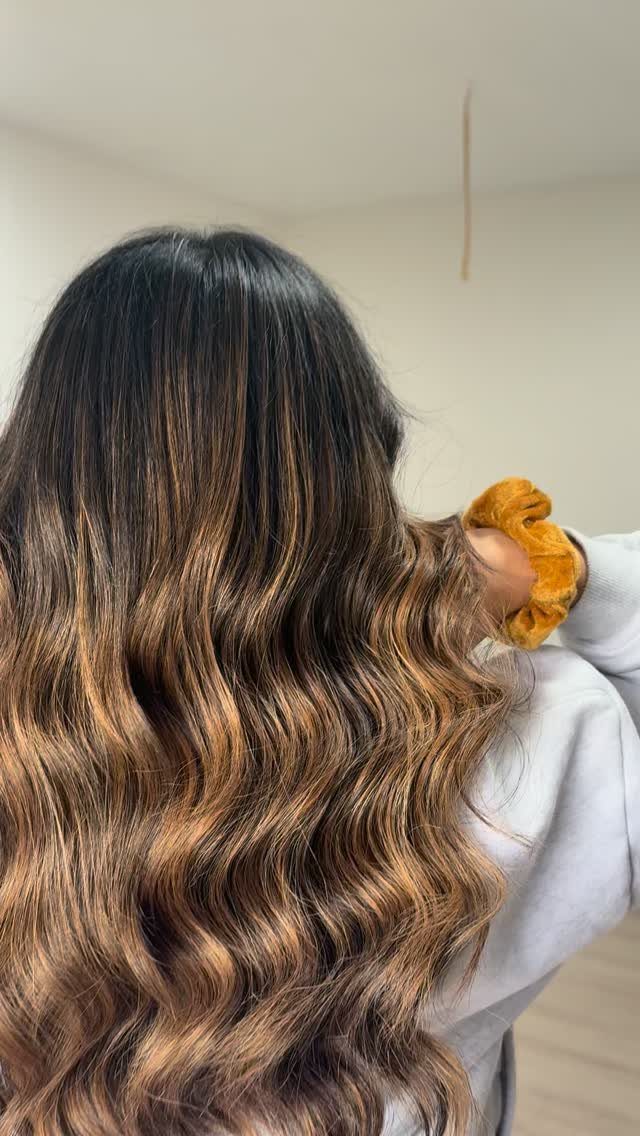 Long wavy brunette hair fades from dark roots to caramel-brown ends