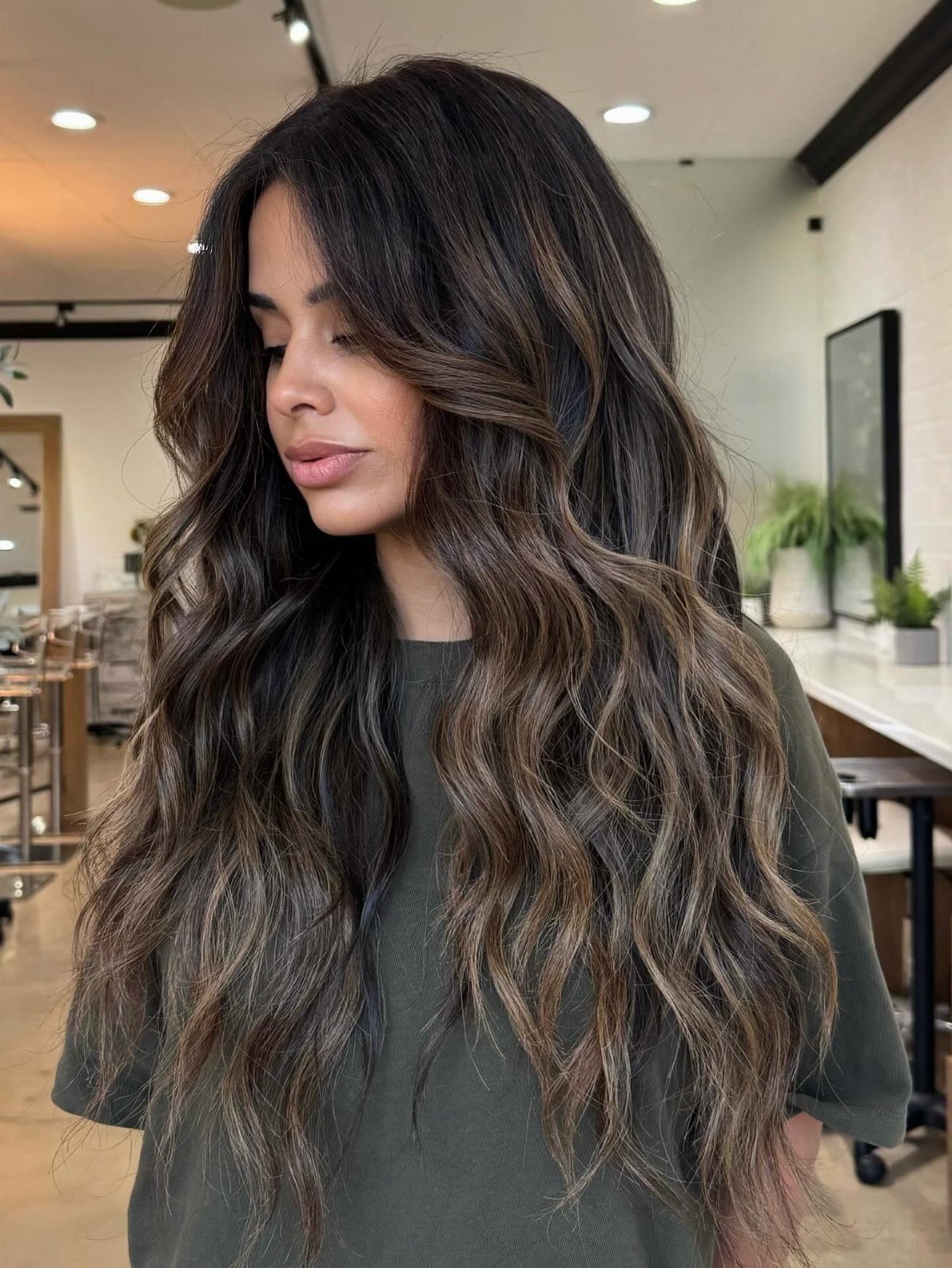 Woman with long brunette waves and lighter face-framing strands in a salon