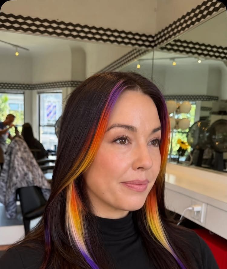 Brunette woman with vivid rainbow highlights framing her face in a salon