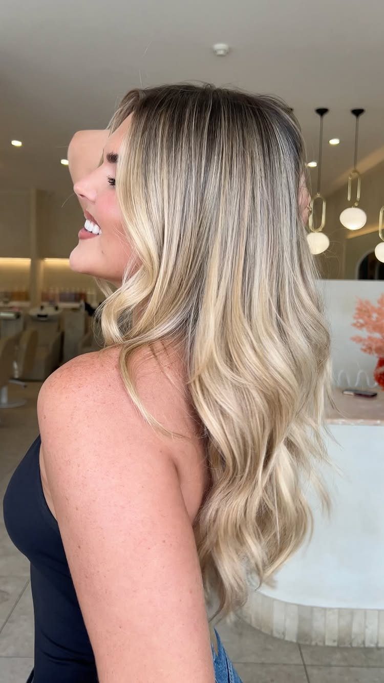 Woman showing long wavy caramel honey blonde hair with darker natural roots