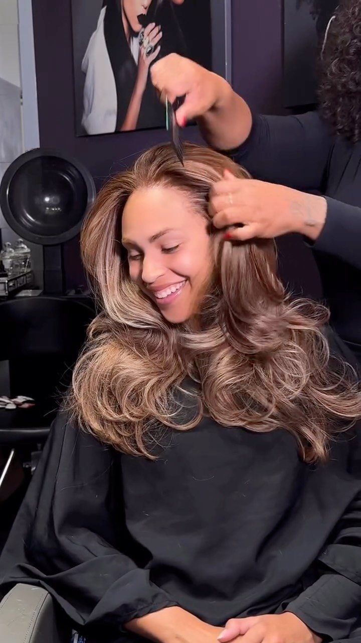 Woman with dark-rooted honey-blonde waves getting her hair styled in a salon