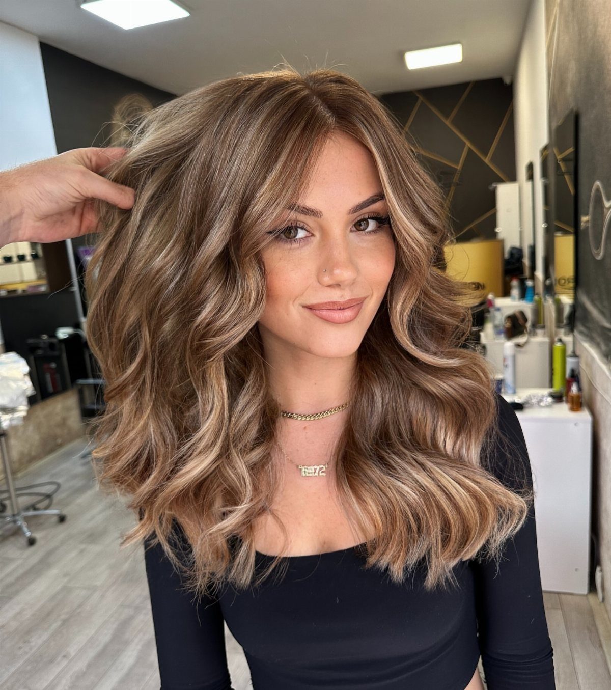 Woman showing wavy honey bronde hair with warm highlights in a salon