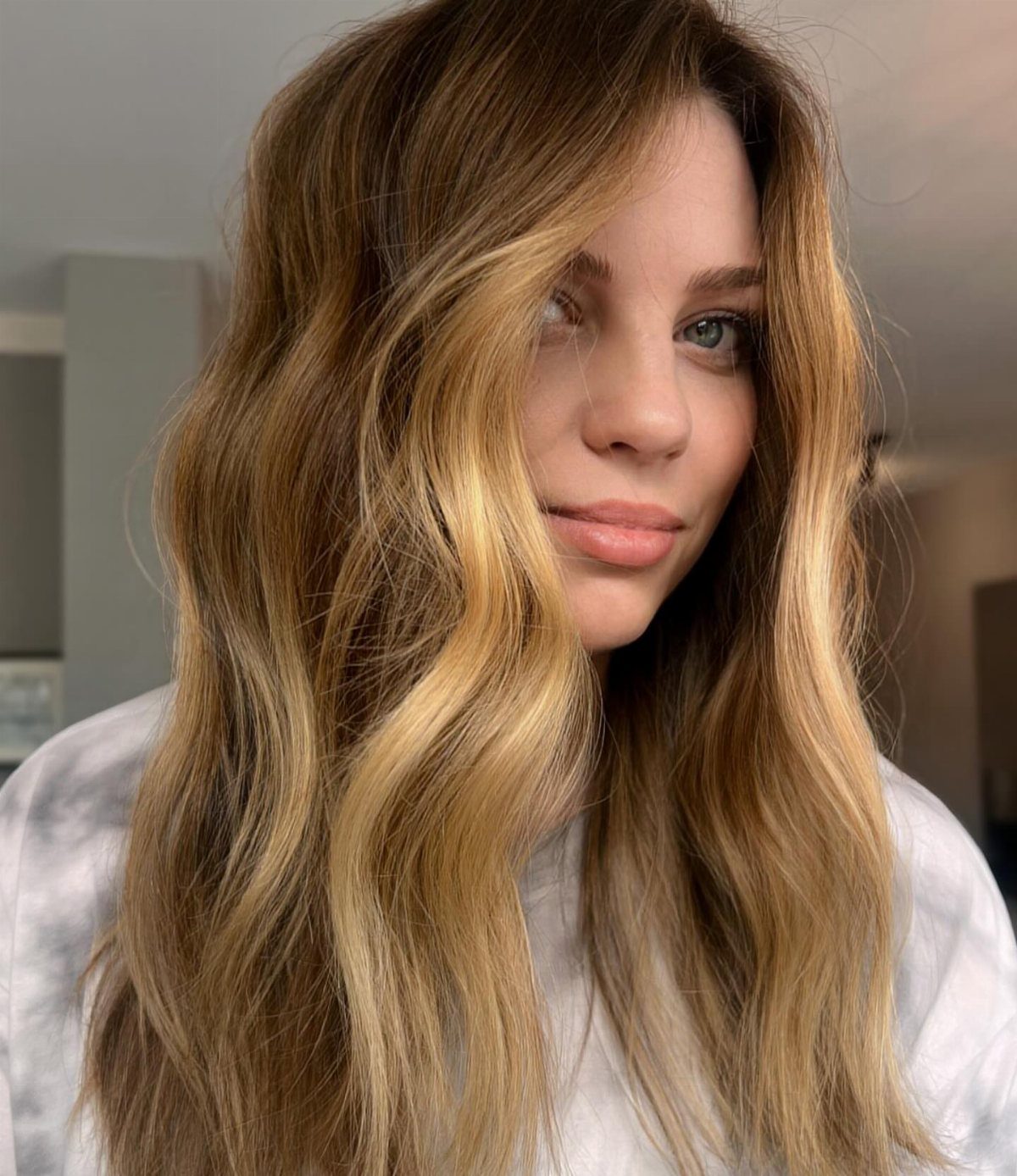 Woman with long wavy dark blonde hair and honey highlights framing her face