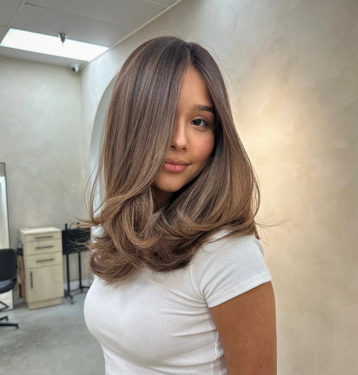 Woman showing layered brown hair with warm blonde highlights and lighter curled ends