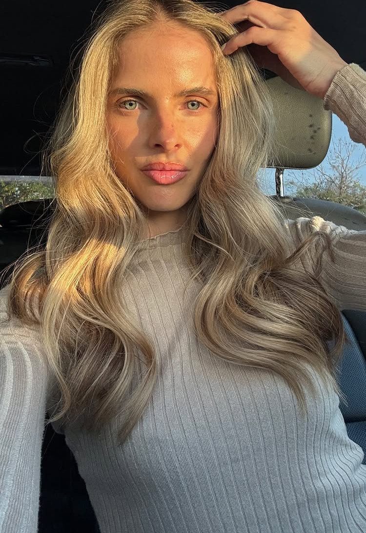 Woman with long, creamy honey blonde waves and darker roots