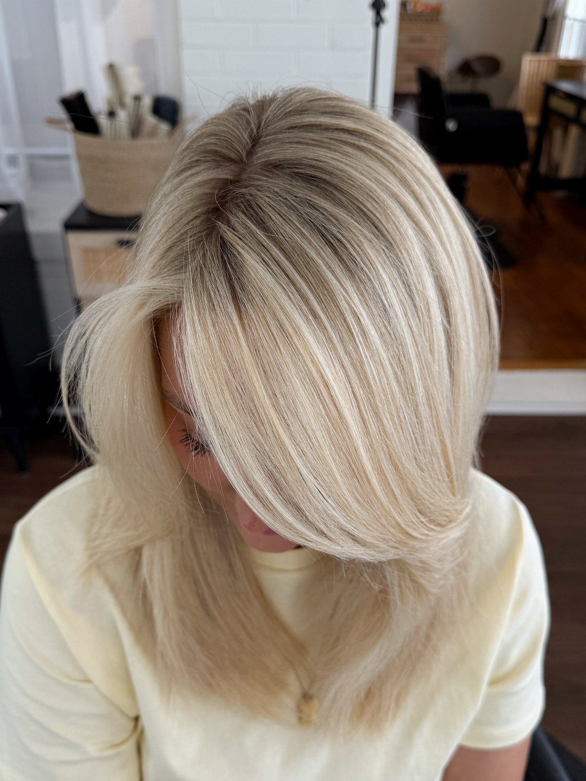 Light blonde shoulder-length hair with darker shadow roots in a salon