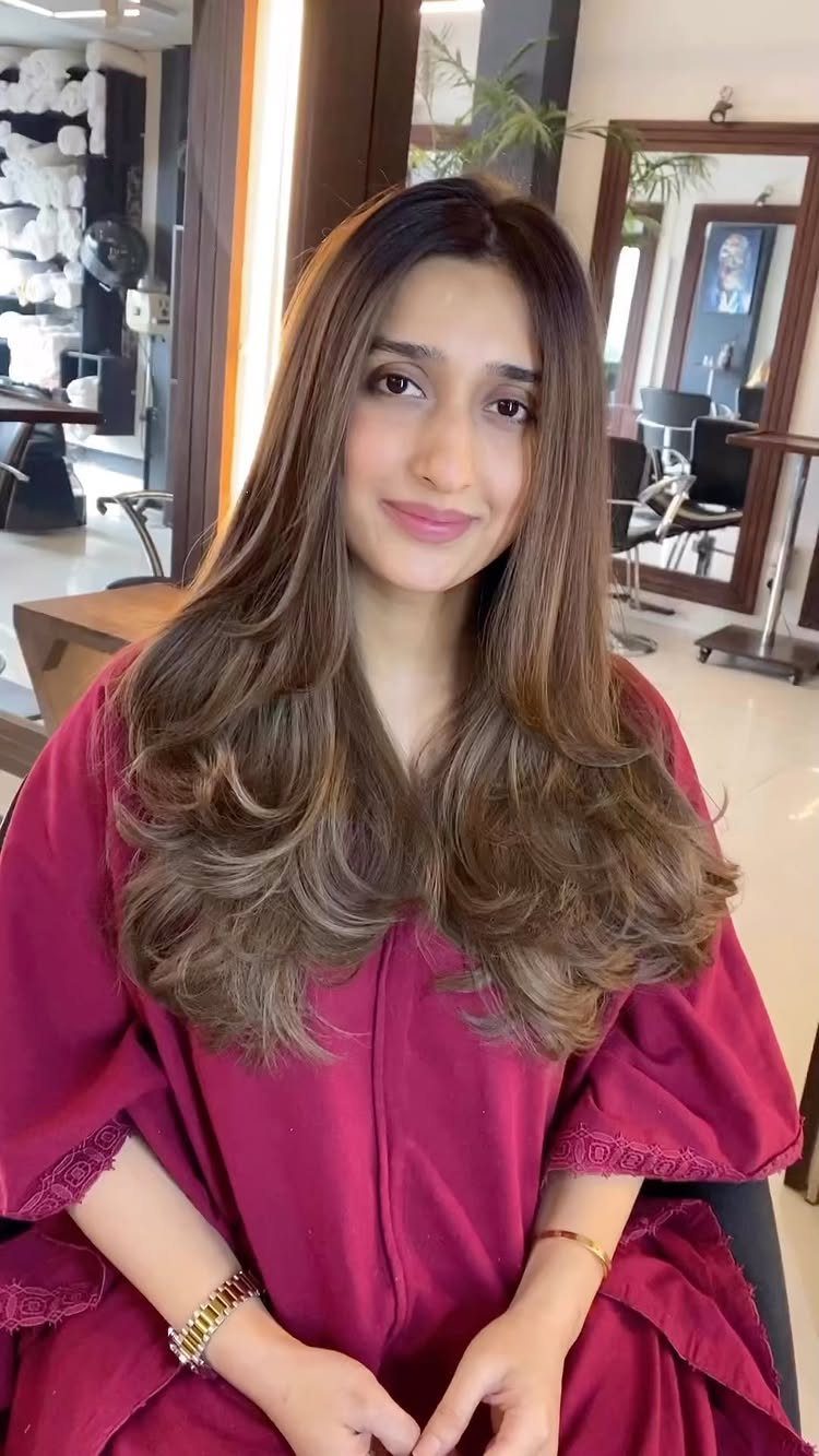 Woman with long brown balayage hair and honey blonde tones seated in a salon