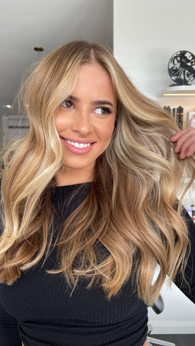 Woman showing long blonde waves with warm caramel lowlights in a salon