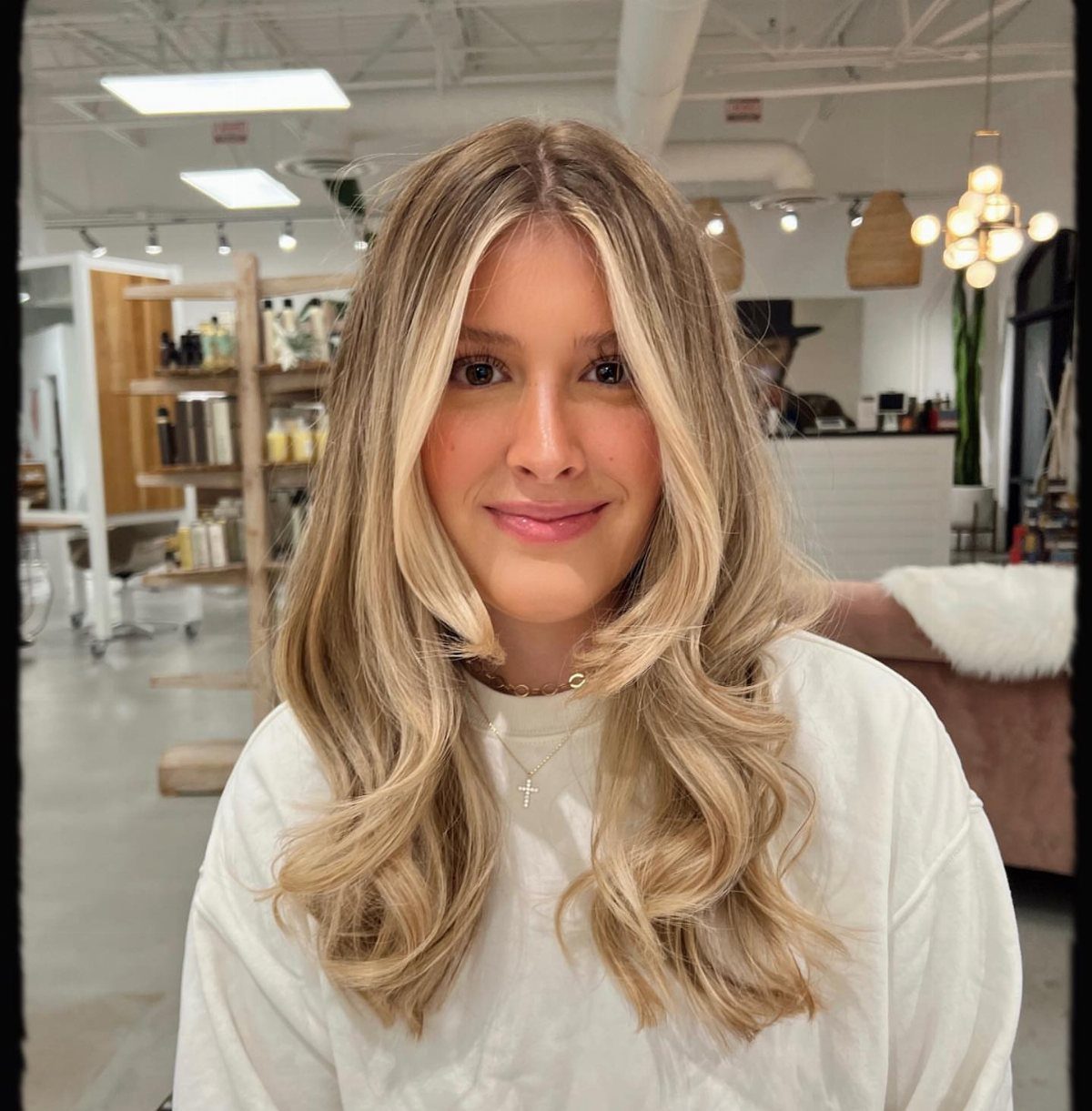 Woman displaying long honey-blonde waves with dimensional brown lowlights in a salon