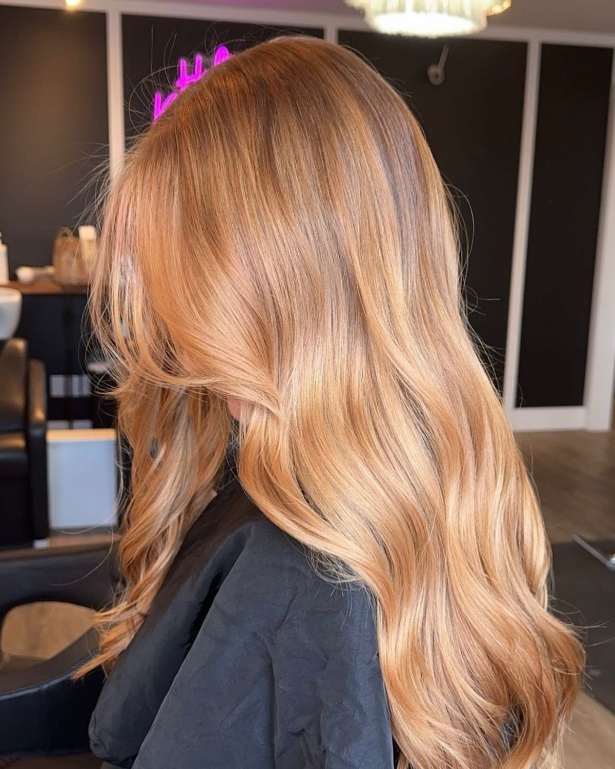 Long wavy strawberry-blonde hair with darker roots in a salon