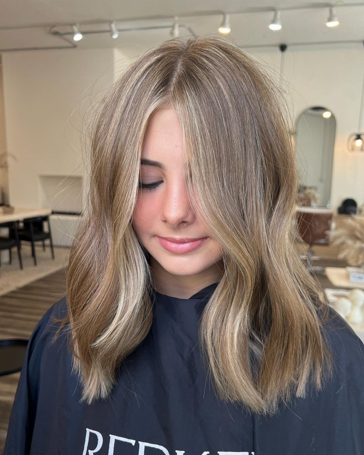 Woman showing softly waved brown hair with subtle blonde highlights in a salon