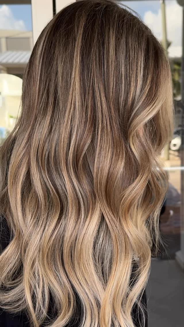Long wavy brown hair with soft blonde highlights and blended dark roots