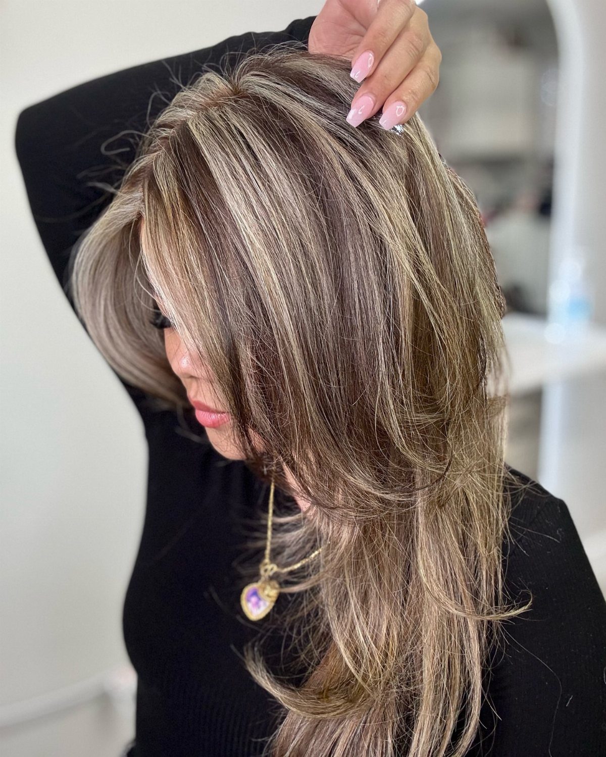 Long brown hair with fine blonde highlights parted at the crown in a salon