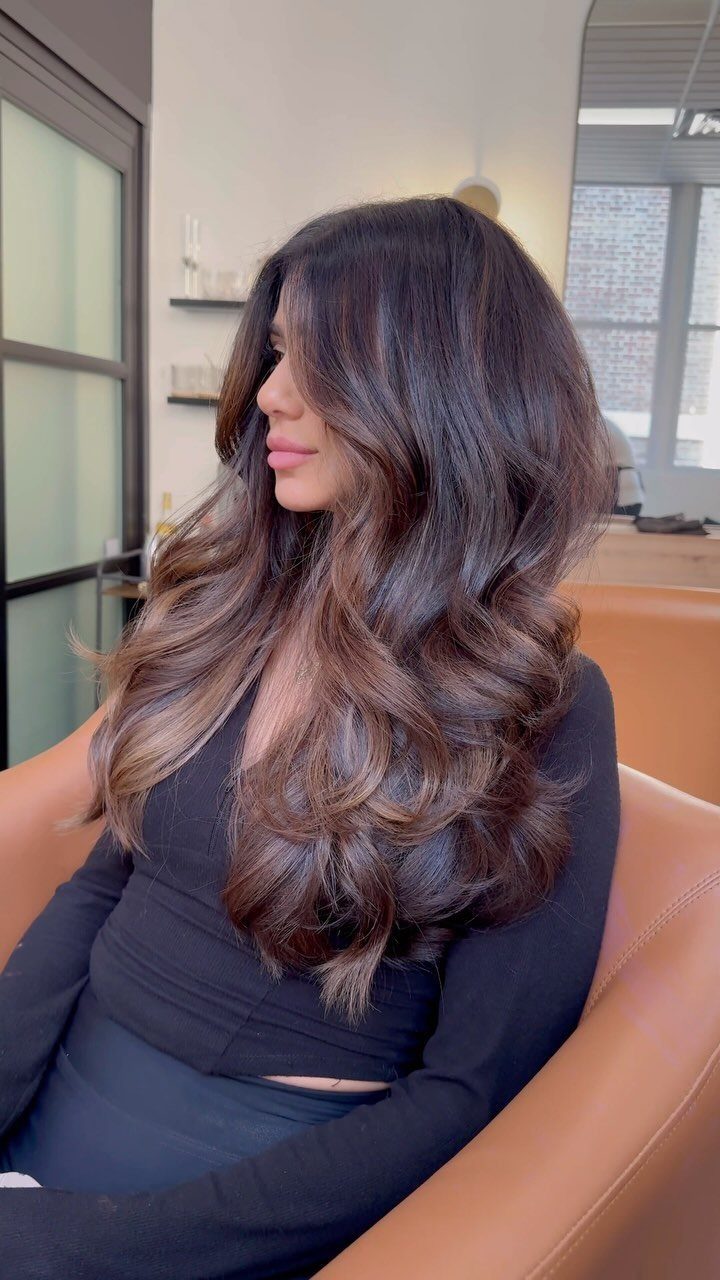 Woman with long, wavy brown hair and subtle lighter highlights seated in a salon chair