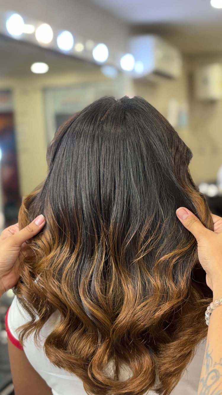 Wavy brunette hair fading into caramel tones at the ends in a salon
