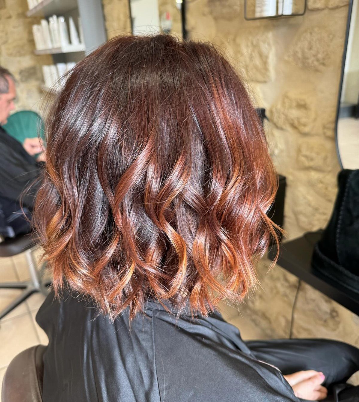 Short wavy brown hair with reddish caramel balayage highlights in a salon