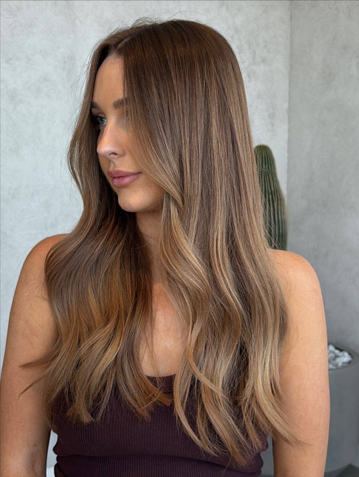Woman with long wavy brown hair fading from dark roots to warm caramel lengths