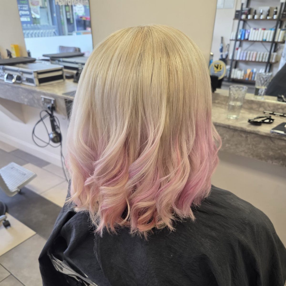 Blonde shoulder-length hair blending into blush-pink curled ends in a salon