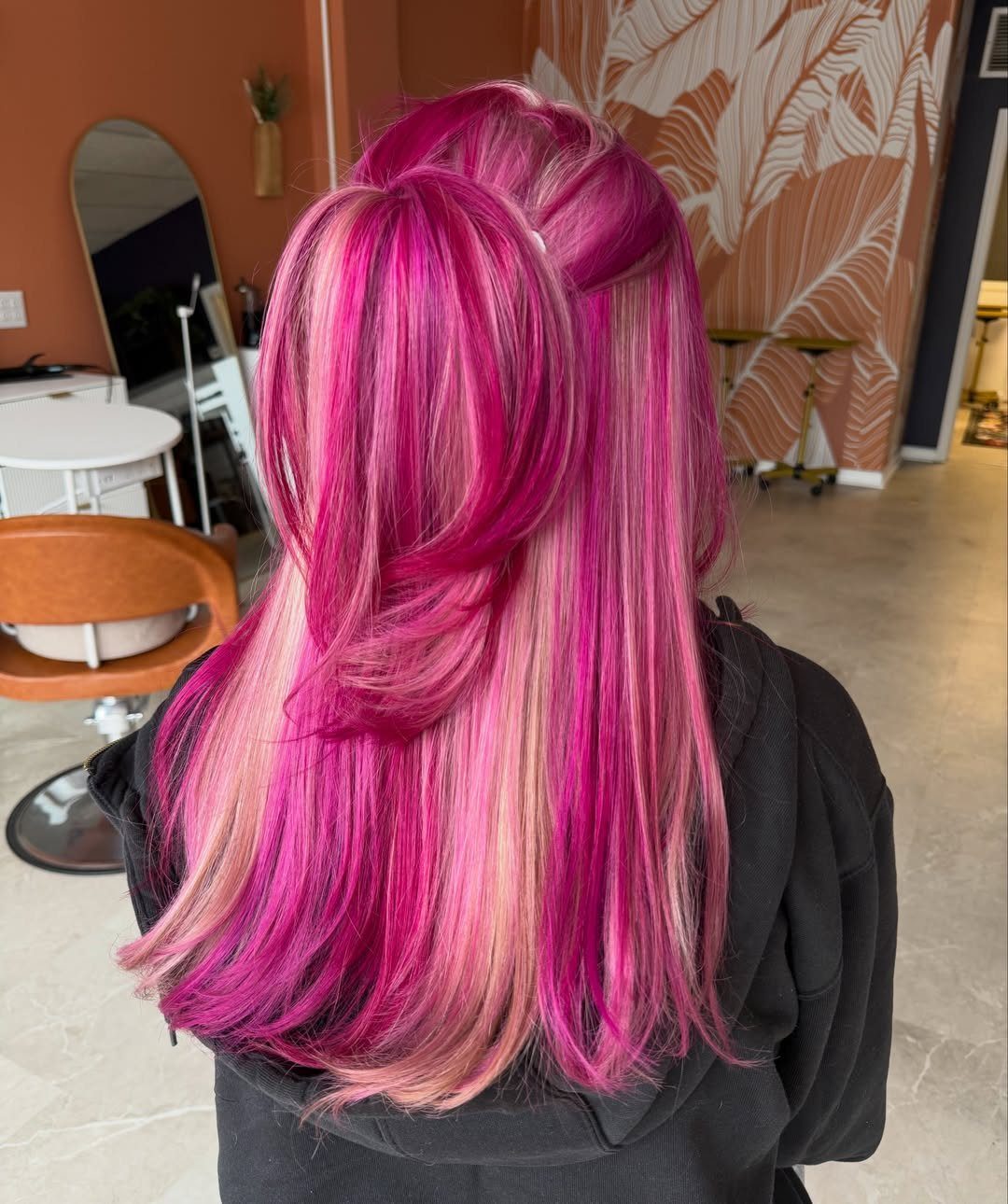 Long layered hair with vivid magenta, pink, and blonde streaks in a salon