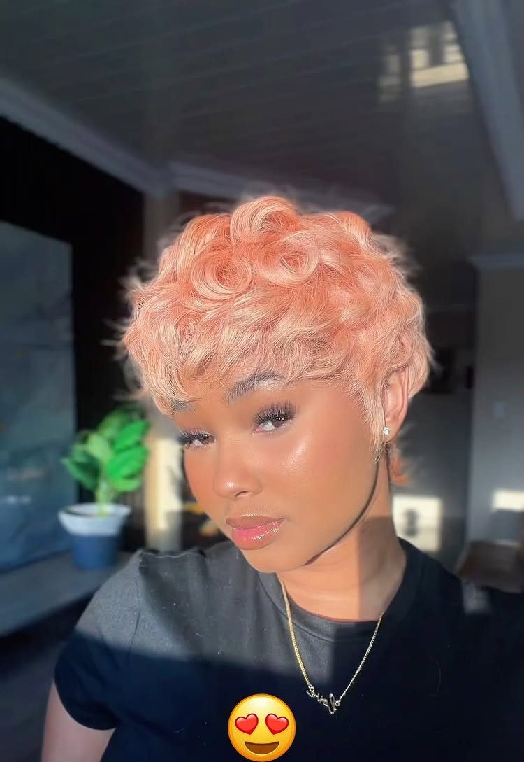 Person posing with a short, curly coral pixie cut and black shirt
