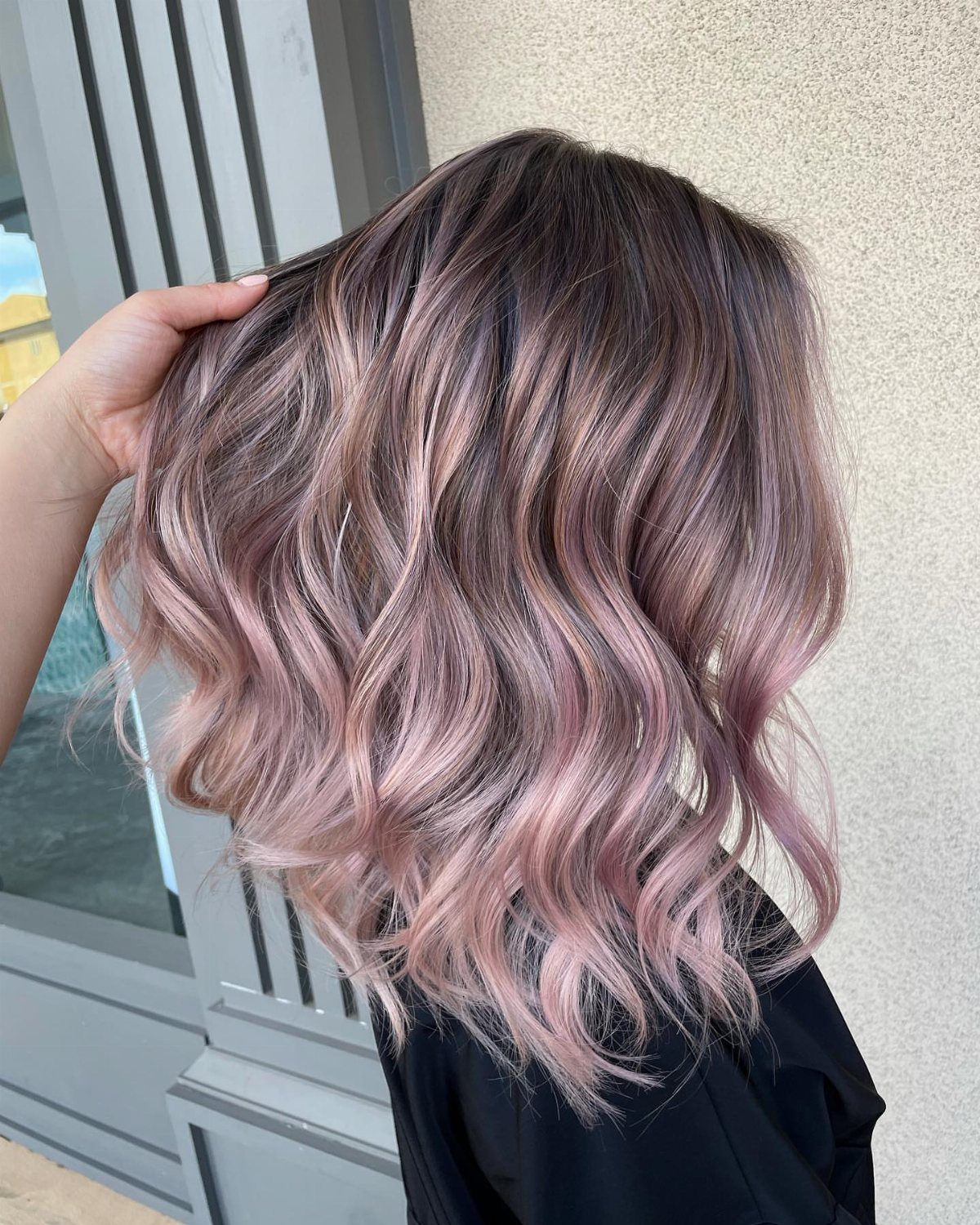 Wavy dark hair with dusty rose highlights held up against a gray doorway