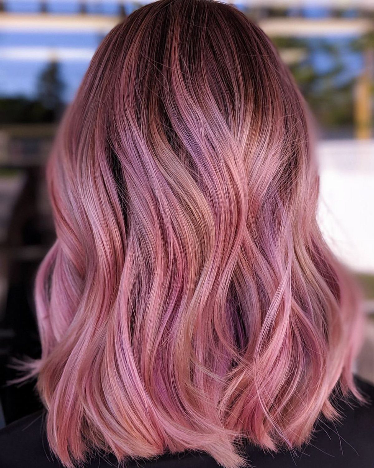 Wavy hair blending dark roots into pastel rose and lilac-purple lengths