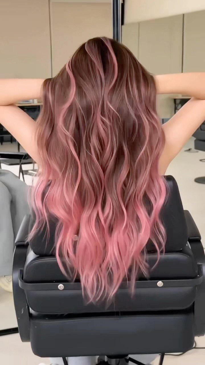 Wavy dark hair blending into pink lengths in a salon chair
