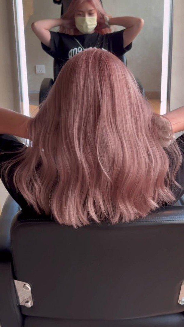 Wavy rose-pink hair with pale highlights drapes over a salon chair