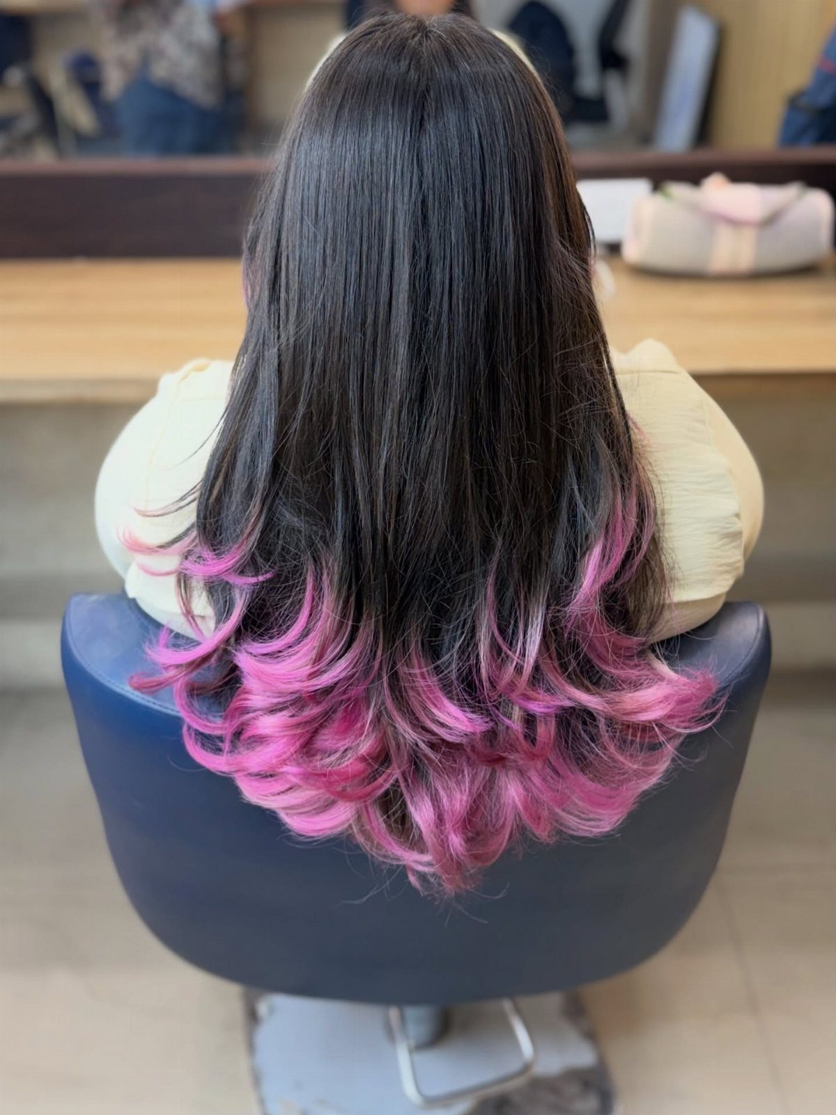 Dark hair fading into vivid pink curled ends in a salon chair