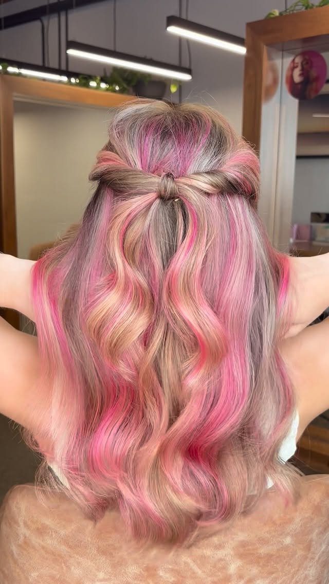 Long blonde waves with strawberry-pink ribbons styled half-up in a salon